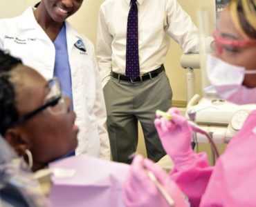 Clifton Bush observes Dr. Shayla Browner (DMD ‘15) and hygienist Ashley Scott (BS Dental Hygiene ‘12). Photo by Todd Stone.