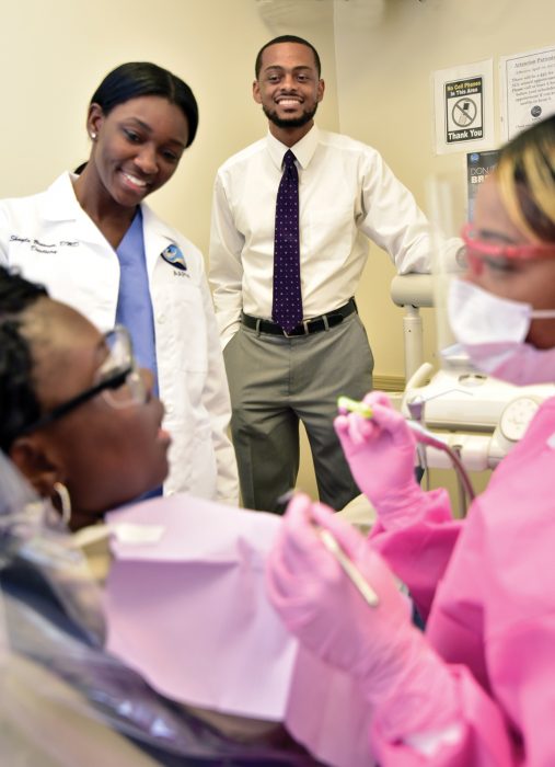 Clifton Bush observes Dr. Shayla Browner (DMD ‘15) and hygienist Ashley Scott (BS Dental Hygiene ‘12). Photo by Todd Stone.