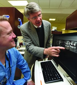 Dentist pointing at x-ray with a man at a keyboard