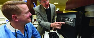 Dentist pointing at x-ray with a man at a keyboard