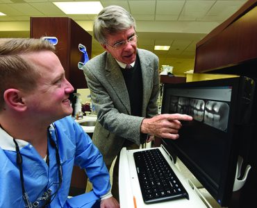 Dentist pointing at x-ray with a man at a keyboard