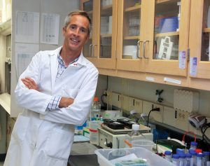 man standing for photo in a lab with arms folded smiling