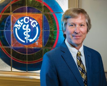 man standing in front of stained glass window with MCG on it