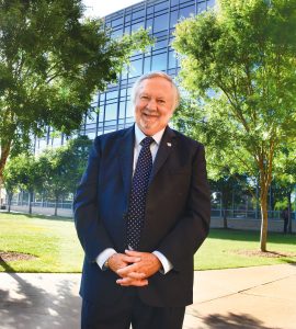 man smiling into camera standing outside in front of a building and trees