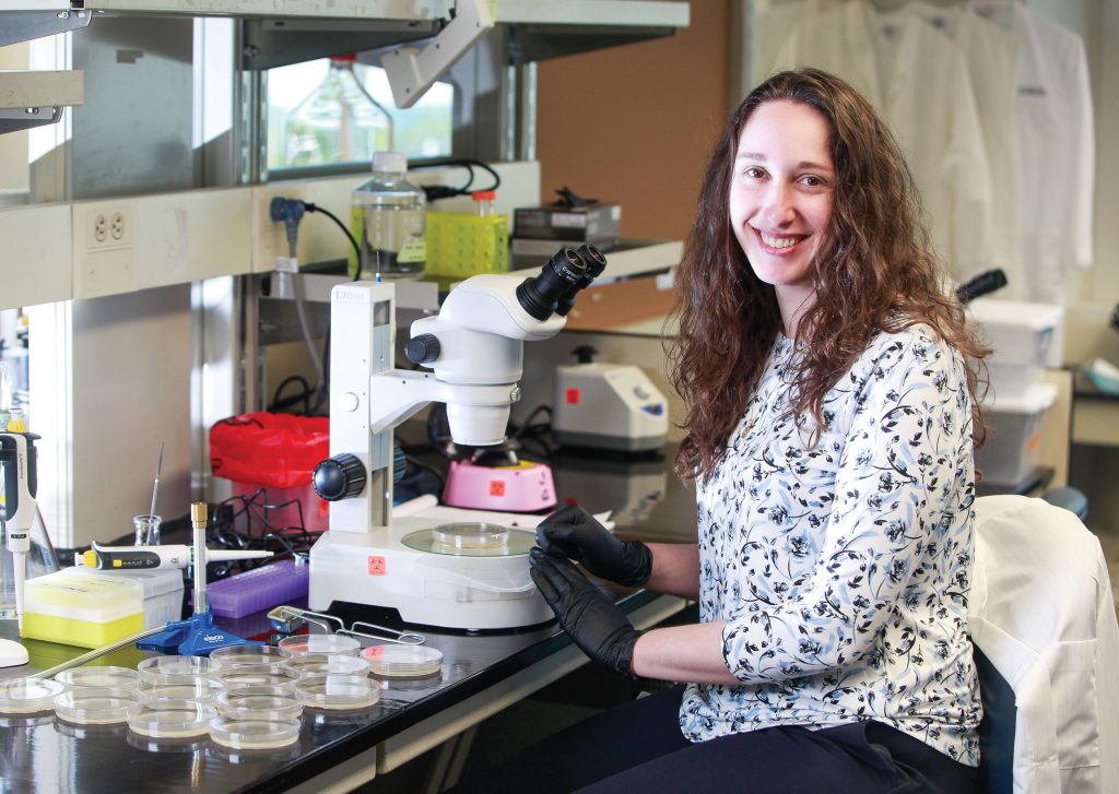 woman sitting in front of microscope turned to smile at camera