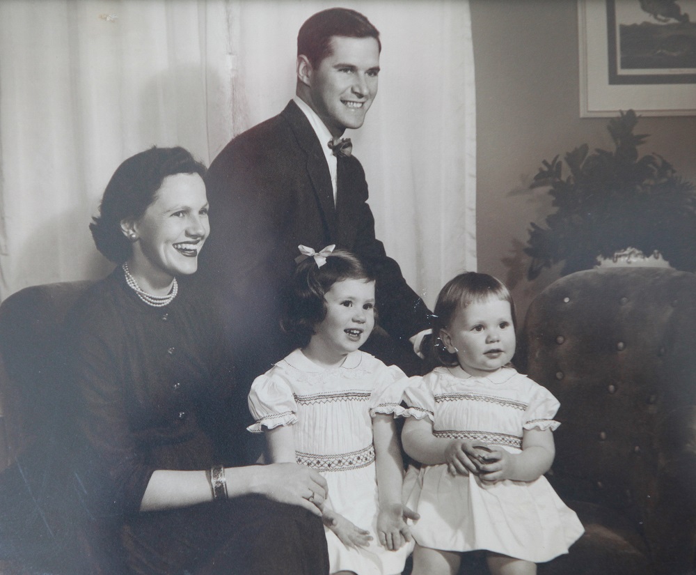 older photo of smiling man, woman and two girls posing for camera