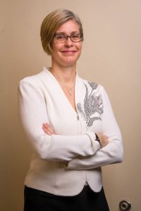 women with arms folded stands smiling