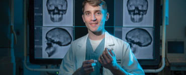 man stands in lab posing for camera in front of x-rays of a skull