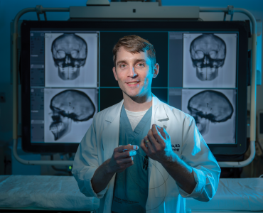 man stands in lab posing for camera in front of x-rays of a skull