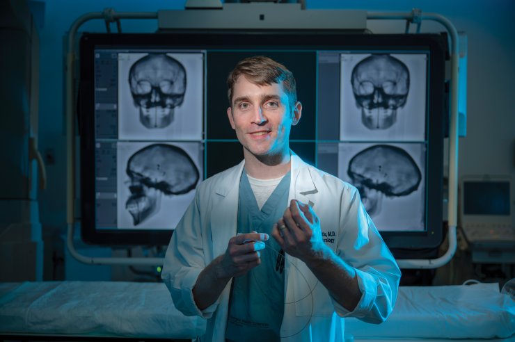 man stands in lab posing for camera in front of x-rays of a skull
