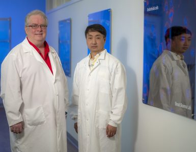 Two men pose for camera in lab