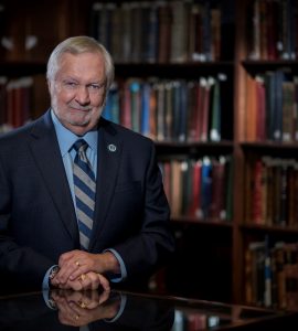 President Brooks A. Keel, PhD poses for camera in front of shelves of books.