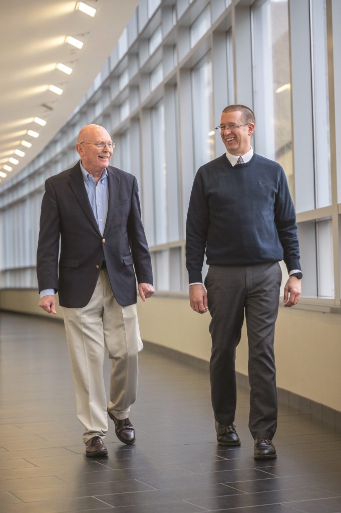 Two men walking in a hallway talking to one another