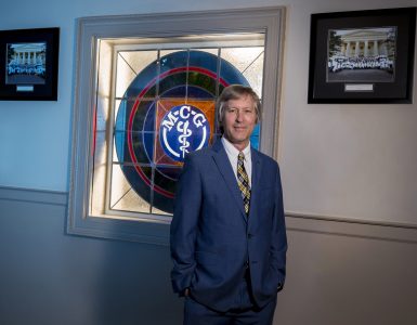 Dr. David Hess stands in front of the MCG stained glass window in the Kelly Building.