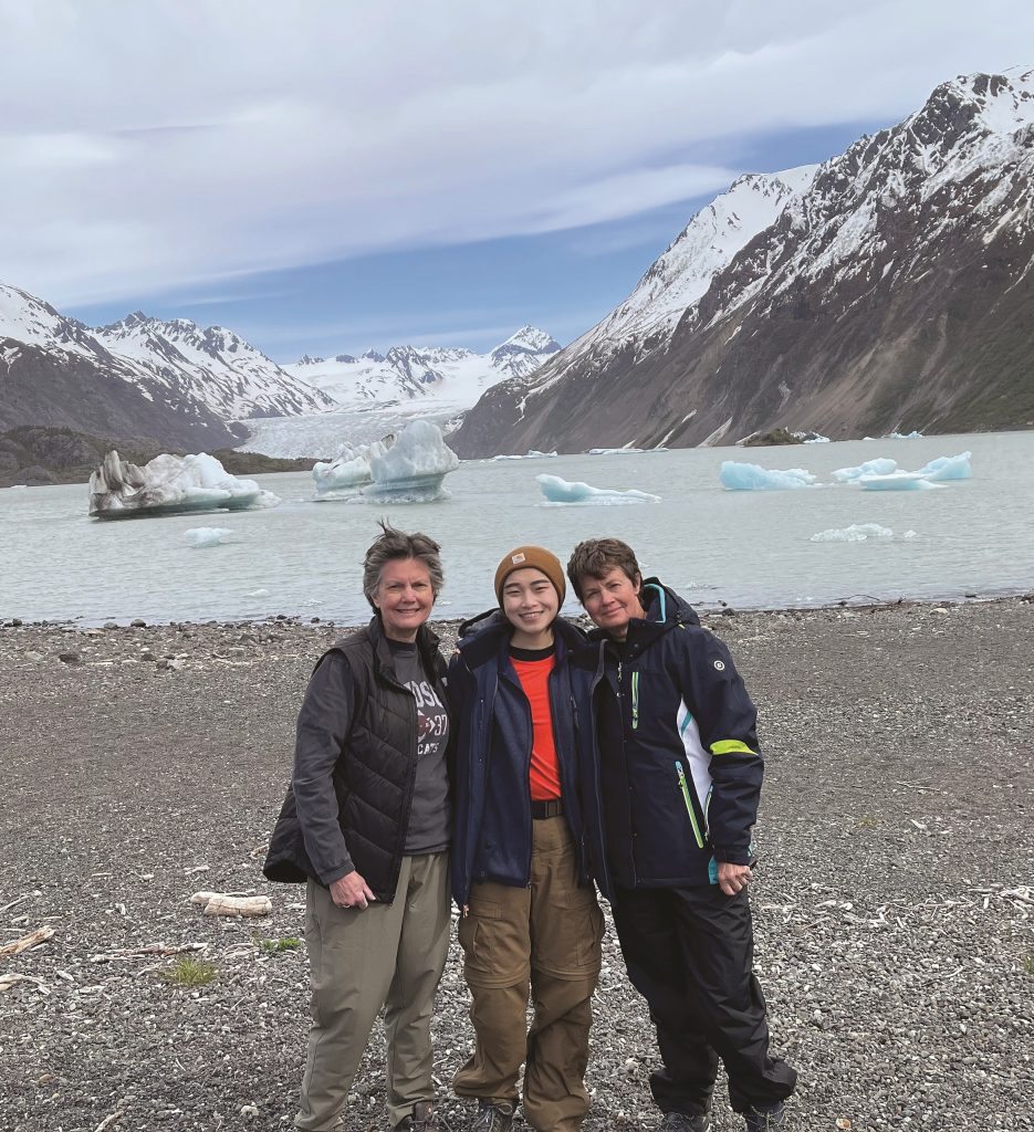 Three women stand in front of the Alaskan wilderness.