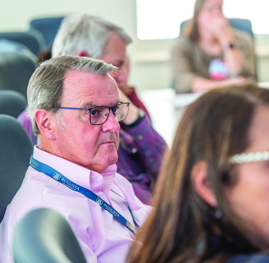 Man listens during a meeting, surrounded by other attendees.