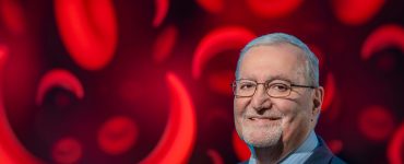 Man smiles at camera with image of red blood cells and sickle cells behind him.