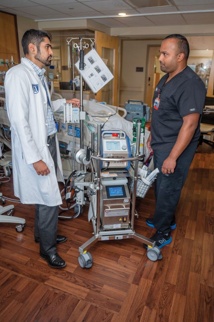 two individuals talking with ECMO machine in middle of page
